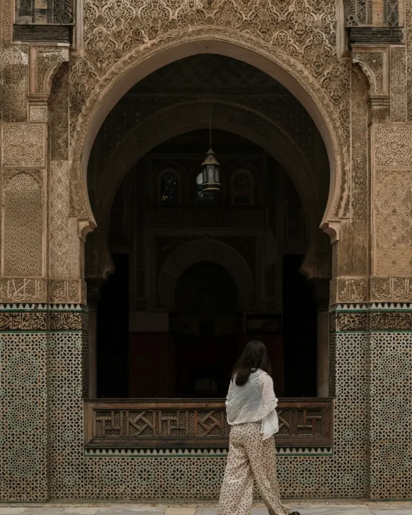 Mujer explorando una madrasa marroquí con arquitectura tradicional