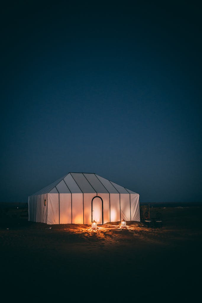 A serene night scene of a glowing tent in the Sahara Desert under a starry sky.