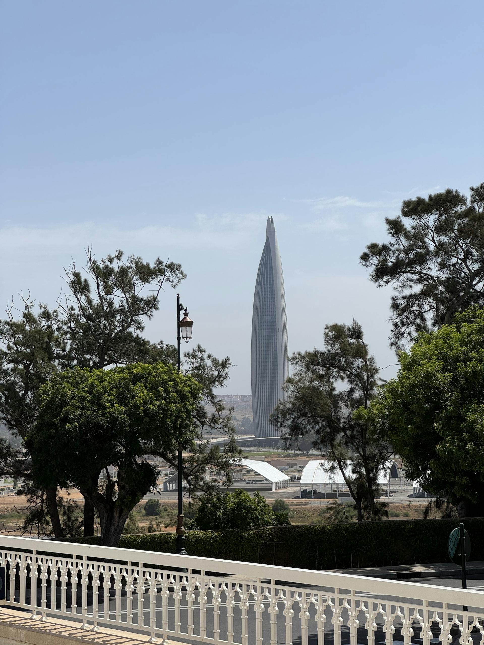 A tall, sleek skyscraper in Rabat, Morocco framed by lush greenery under a clear sky.