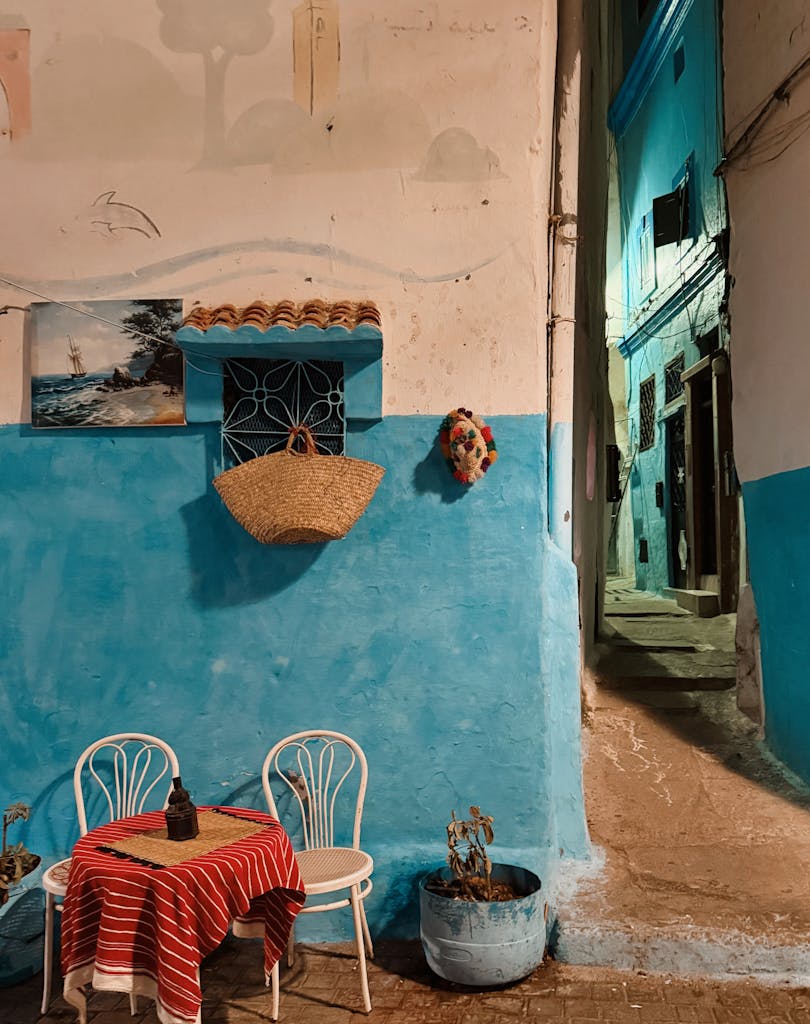Cozy alleyway scene in Larache, Morocco featuring vibrant blue walls, a small table, and night ambiance.