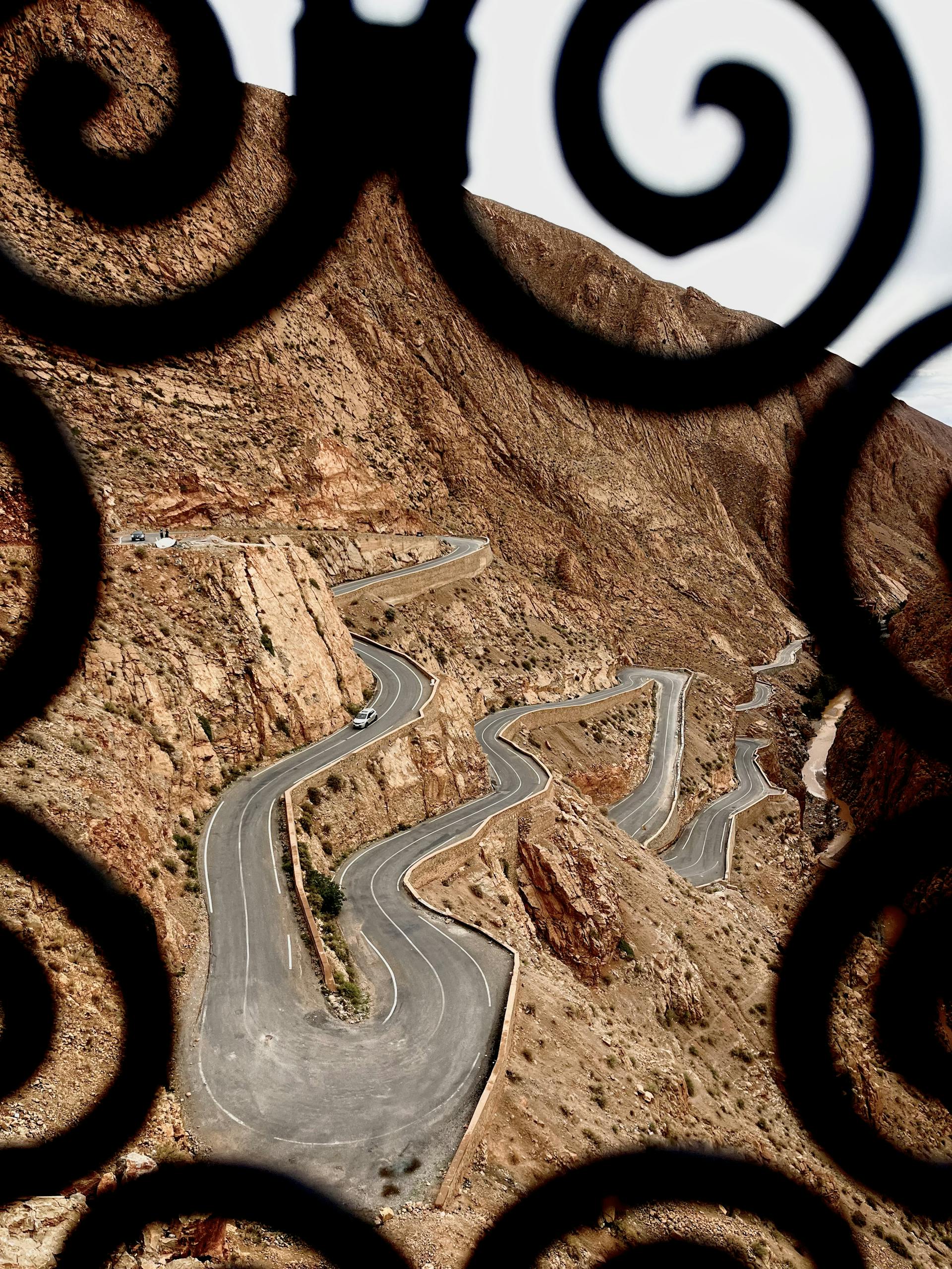 Scenic view of a winding road through the Atlas Mountains framed by ornate ironwork.