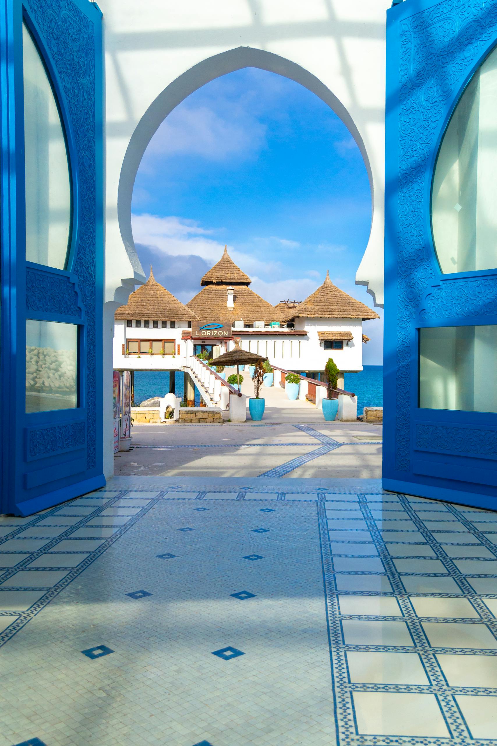 View through ornate Moroccan doors towards a coast, showcasing traditional architecture and sea.